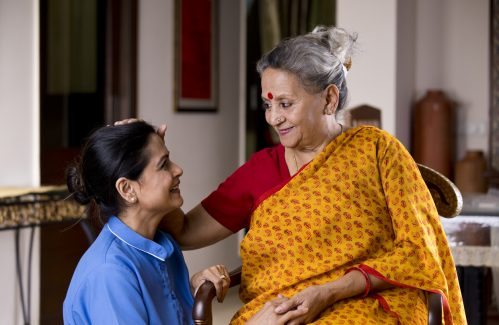 Happy old woman giving blessings to female nurse at home
